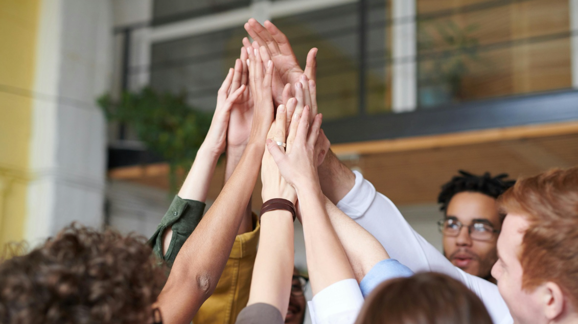 Diverse workplace team raising hands together to celebrate inclusion and collaboration